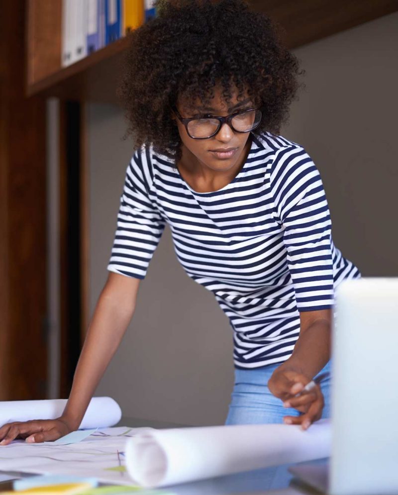 woman-reviewing-blueprints-with-laptop-in-workplac-2026-03-25-06-32-30-utc
